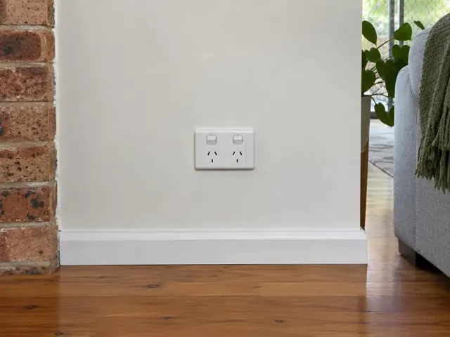 Double power point on a white wall above skirting beside brick and timber flooring in Pacific Pines