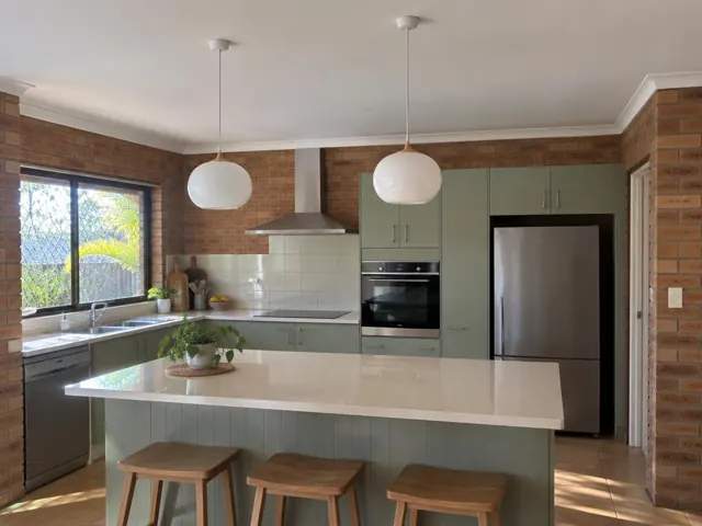 Two white pendant lights over a kitchen island in a brick home interior in Oxenford