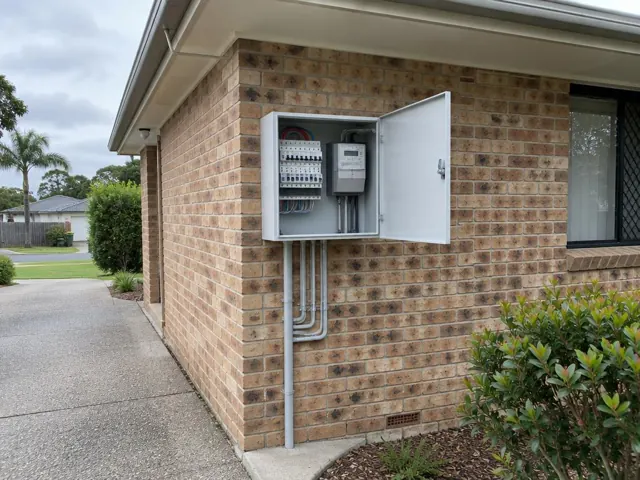 Open switchboard and meter box on an exterior brick wall beside a driveway in Maudsland